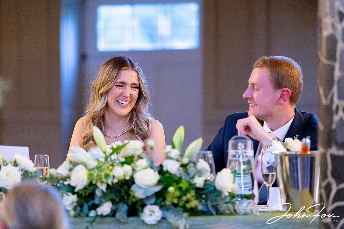 Lorna and James laughing together at the top table during their wedding celebrations at Chicheley Hall.