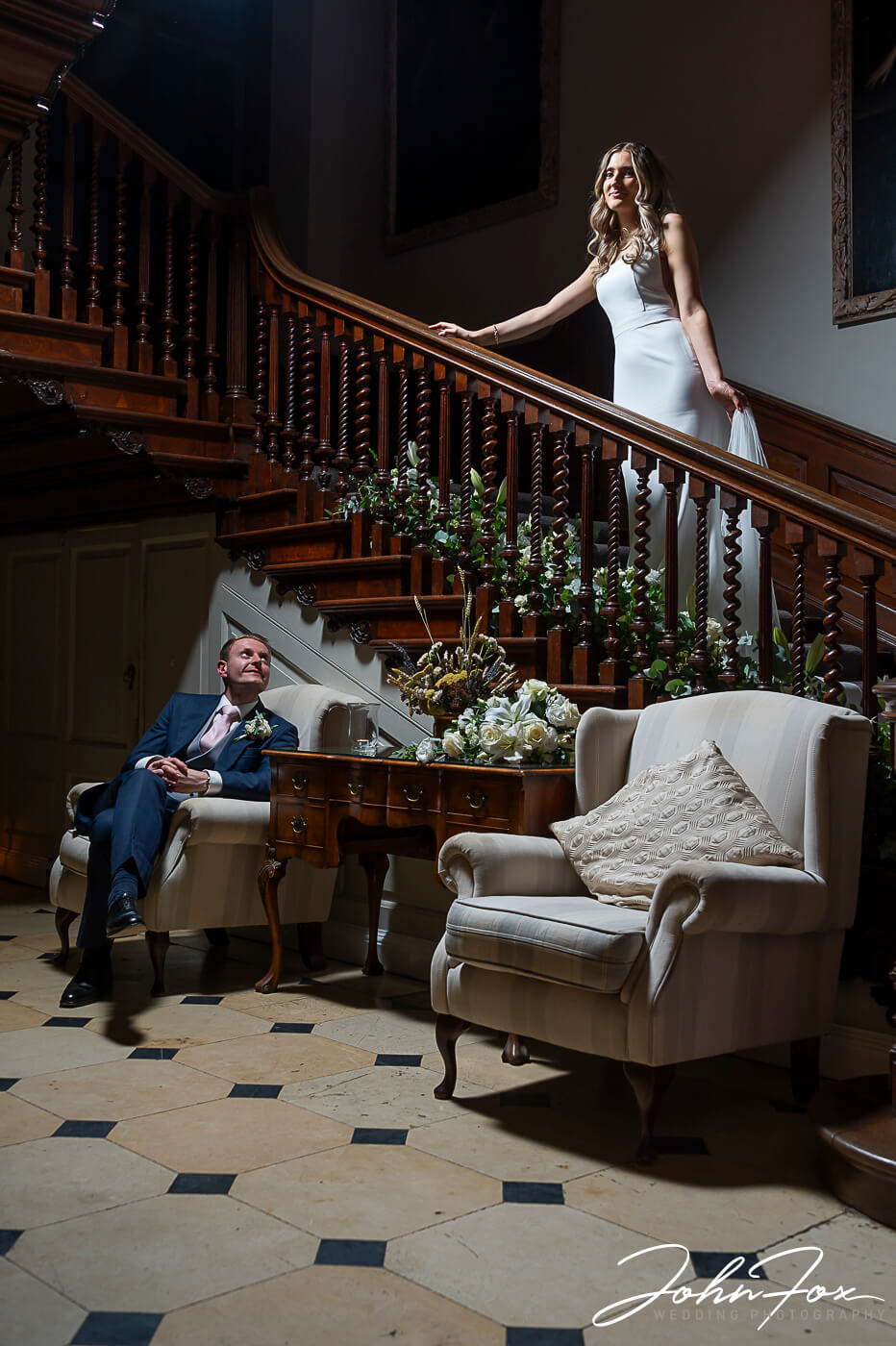 Lorna on the grand staircase at Chicheley Hall with James looking up at her from a seat in the hall