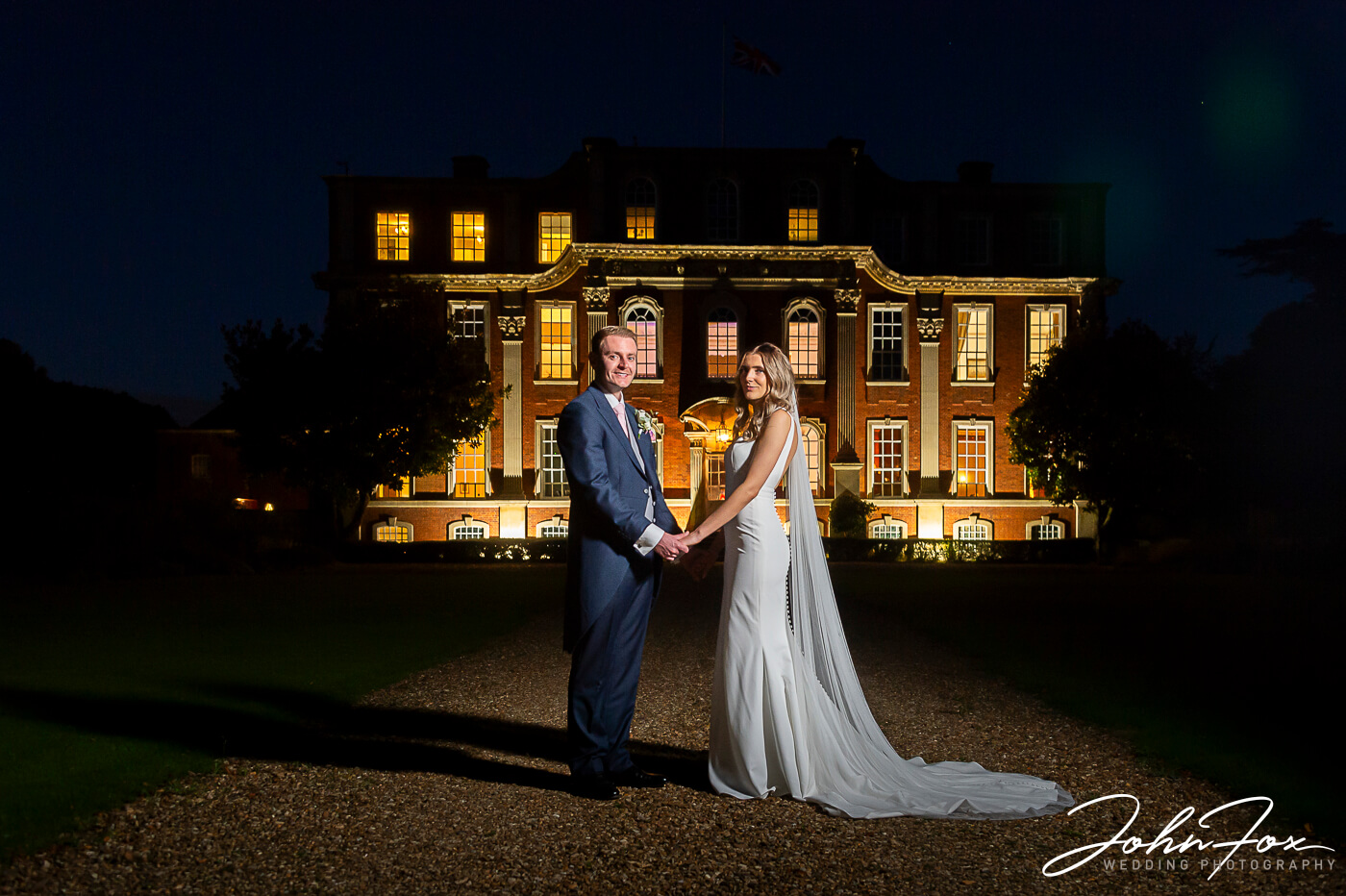 Lorna and James outside Chicheley Hall in Buckinghamshire on their wedding evening with the magnificent venue lit up behind them